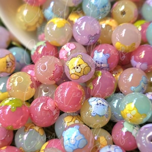 May include: A collection of colorful, translucent round beads in shades of pink, yellow, blue, and purple. Each bead features a cartoon bear illustration. The beads are scattered, creating a playful and whimsical aesthetic.