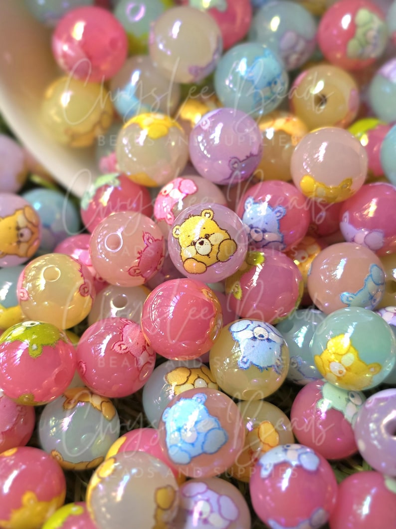 May include: A collection of colorful, translucent round beads in shades of pink, yellow, blue, and purple. Each bead features a cartoon bear illustration. The beads are scattered, creating a playful and whimsical aesthetic.