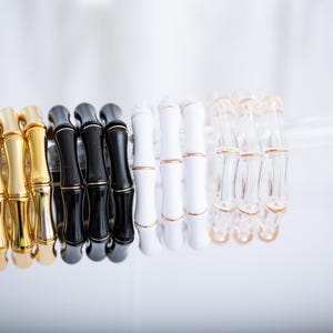 May include: Four sets of stacked bamboo bracelets in gold, black, white, and clear. Each bracelet is made of multiple pieces of bamboo connected by gold rings.