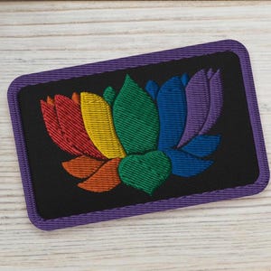 May include: A purple embroidered patch with a rainbow lotus flower design. The lotus flower is made up of six petals in the colors of the rainbow.