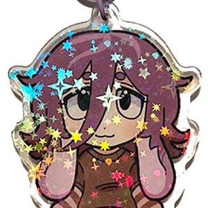 May include: A clear acrylic charm featuring a cartoon character with purple hair and a brown shirt. The charm has a star-shaped clasp and is decorated with holographic glitter and star accents. The character is wearing blue jeans and checkered shoes.