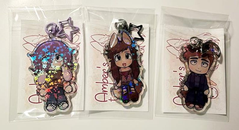May include: Three clear acrylic keychains featuring anime-style characters. Each keychain has a different character design, with holographic accents. The keychains are packaged in clear plastic bags.