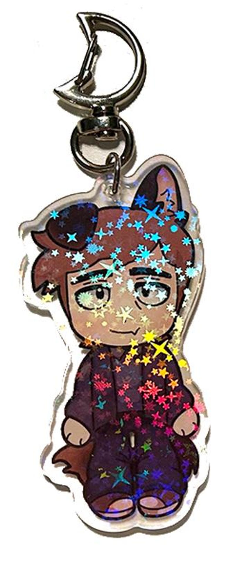 May include: A clear acrylic keychain featuring a cartoon character with brown hair, cat ears, and a purple outfit. The design is decorated with holographic star-shaped accents and a silver metal clasp.