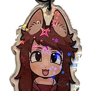 May include: A clear acrylic keychain featuring a cartoon character with brown hair, large eyes, and a fox-like appearance. The keychain has a black star-shaped clasp and is decorated with holographic accents.
