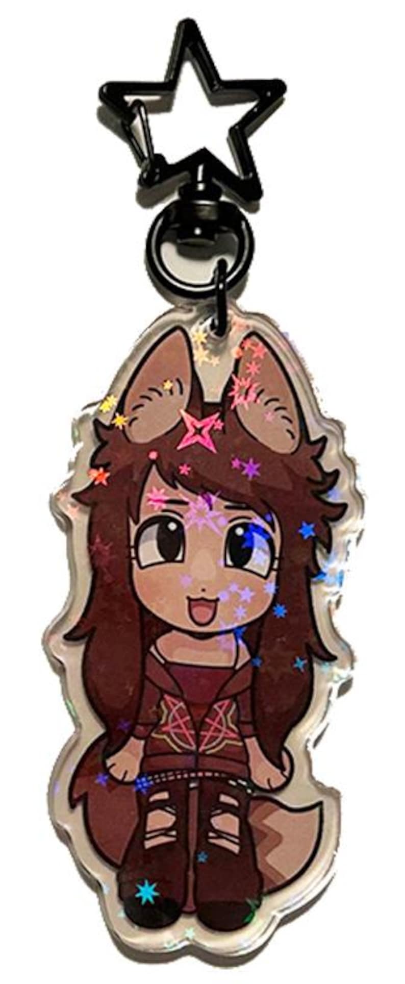 May include: A clear acrylic keychain featuring a cartoon character with brown hair, large eyes, and a fox-like appearance. The keychain has a black star-shaped clasp and is decorated with holographic accents.