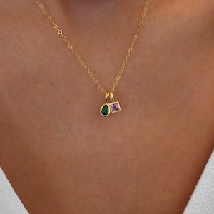 May include: A gold chain necklace with two small charms. One charm is a teardrop-shaped green gemstone, and the other is a square pink gemstone.