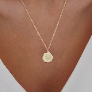May include: A gold chain necklace with a delicate pendant featuring a sunburst design with a small diamond in the center.