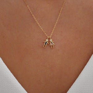 May include: A gold chain necklace with a pendant featuring two small figures holding hands. The figures have small gemstones for heads, one blue and one pink.
