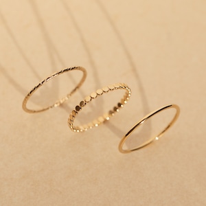 Puede incluir: Tres anillos de oro, uno con una superficie texturizada, otro con un diseño de cuentas y otro con una superficie lisa.