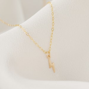 May include: A gold chain necklace with a small lightning bolt pendant.