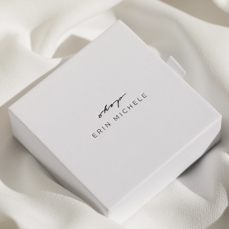 May include: White square box with the text "shop erin michele" printed in black.