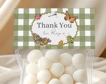 May include: A clear cellophane bag filled with white candies, topped with a green and white checkered label. The label reads "Thank You love Raye" and features butterfly and insect illustrations. The bag sits on a white plate.