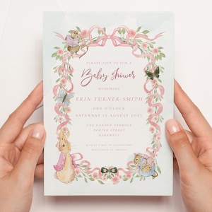 May include: A light blue baby shower invitation with pink ribbon and floral accents. The invitation features illustrations of Peter Rabbit and other woodland creatures. The text reads "Please join us for a Baby Shower honoring Erin Turner-Smith One O'Clock Saturday 12 August 2025 The Garden Terrace Poster Street Rakewell"