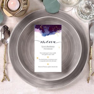 May include: A menu card with a dark blue and purple watercolor background with gold stars and a crescent moon. The text on the card reads "menu", "Celente's Baby Shower", "1 November 2020", "Two baked goat's cheese souffle with apple & walnut salad", "Pan-fried chicken in mushroom sauce on vegetable tartlets with wild salad", "Boerset Panna cotta, apple & almond cake".