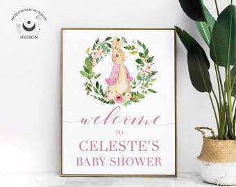May include: A white sign with a brown wooden frame, featuring a watercolor illustration of a rabbit wearing a pink jacket, surrounded by a floral wreath. The text "welcome to CELESTE'S BABY SHOWER" is written in pink cursive lettering.