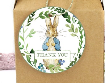 Puede incluir: Etiqueta redonda de agradecimiento con una ilustración de acuarela de Peter Rabbit con una chaqueta azul rodeado de hojas verdes y bayas azules. La etiqueta tiene el texto "THANK YOU" en una pancarta verde.
