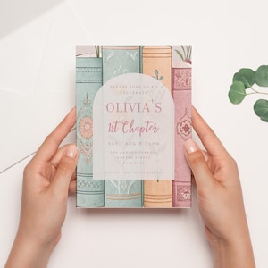 May include: A pastel-colored invitation with a stack of books and floral accents. The text reads "Please join us to celebrate Olivia's 1st Chapter. Sat | Aug 8 | 1 PM. The Garden Terrace, Porter Street, Bakewell. RSVP by May 10, 2023."