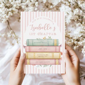 May include: Pink and white striped invitation with a stack of colourful books decorated with flowers. The invitation reads "Join us to celebrate Isabelle's 1st Chapter" with the date, time, and location.