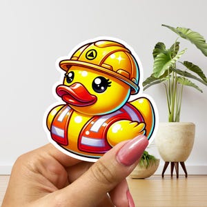 May include: A yellow rubber duck wearing a yellow construction hat and an orange safety vest. The duck has large, black eyes and a red beak.