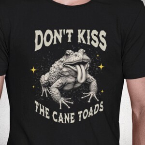 May include: Black t-shirt with a graphic of a toad with its tongue out. The text "DON'T KISS THE CANE TOADS" is arched above and below the toad illustration. Yellow starbursts are on either side of the toad.