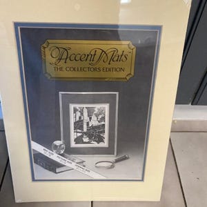May include: A rectangular cream-colored picture mat with a dark blue inner border. The top features a gold label reading Accent Mats THE COLLECTORS EDITION. A white diagonal strip displays text: MAT SIZE 12 x 16, PICTURE SIZE 9 x 12, OPENING SIZE 8.5 x 11.5.
