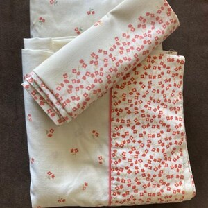 May include: A set of white bed linens with a small red floral pattern. The fitted sheet has a red border.