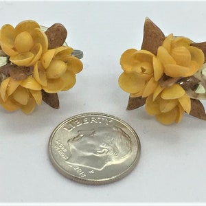May include: A pair of yellow seashell flower earrings with brown accents. The earrings are about the size of a dime.