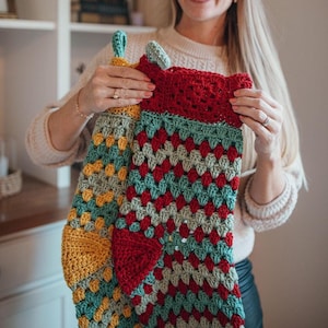 Puede incluir: Dos calcetines de Navidad de ganchillo, uno rojo, verde y turquesa, y otro amarillo, verde y turquesa. Los calcetines los sostiene una persona con el pelo largo y rubio.