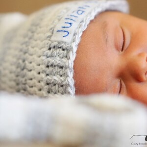 Puede incluir: Un beb&eacute; reci&eacute;n nacido con un gorro de punto gris con el nombre "Julian" bordado. El beb&eacute; duerme pl&aacute;cidamente.