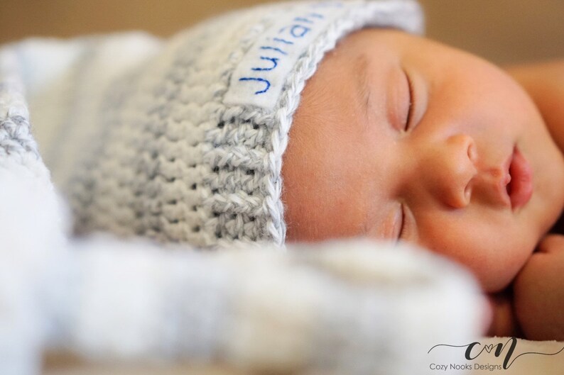 Puede incluir: Un beb&eacute; reci&eacute;n nacido con un gorro de punto gris con el nombre "Julian" bordado. El beb&eacute; duerme pl&aacute;cidamente.