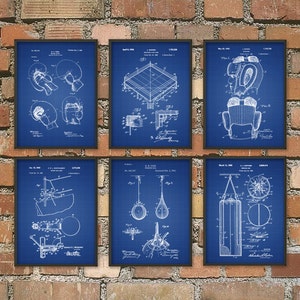 May include: Six framed blue prints of boxing equipment, including gloves, a ring, and a punching bag, are displayed against a brick wall. The blueprints are white line drawings on a blue grid background, with dates and technical details.