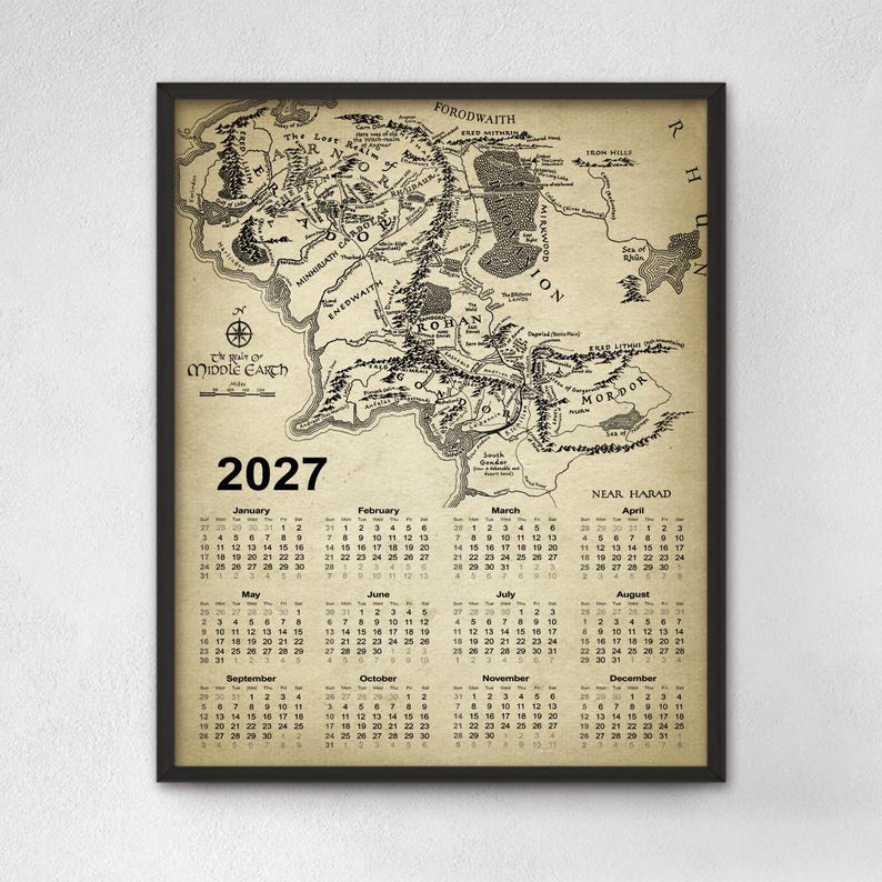 May include: A framed wall calendar for the year 2027 featuring a vintage-style map of Middle-earth. The map displays geographical regions, mountain ranges, and forests in black ink on a tan parchment background. The calendar grid is printed below.