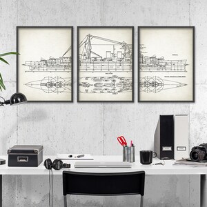 K&ouml;nnte beinhalten: Drei schwarze gerahmte Drucke eines Schiffsbauplans an einer wei&szlig;en Wand &uuml;ber einem wei&szlig;en Schreibtisch mit einer schwarzen Lampe, einer schwarzen Box, einer Kamera und einem schwarzen Stuhl.