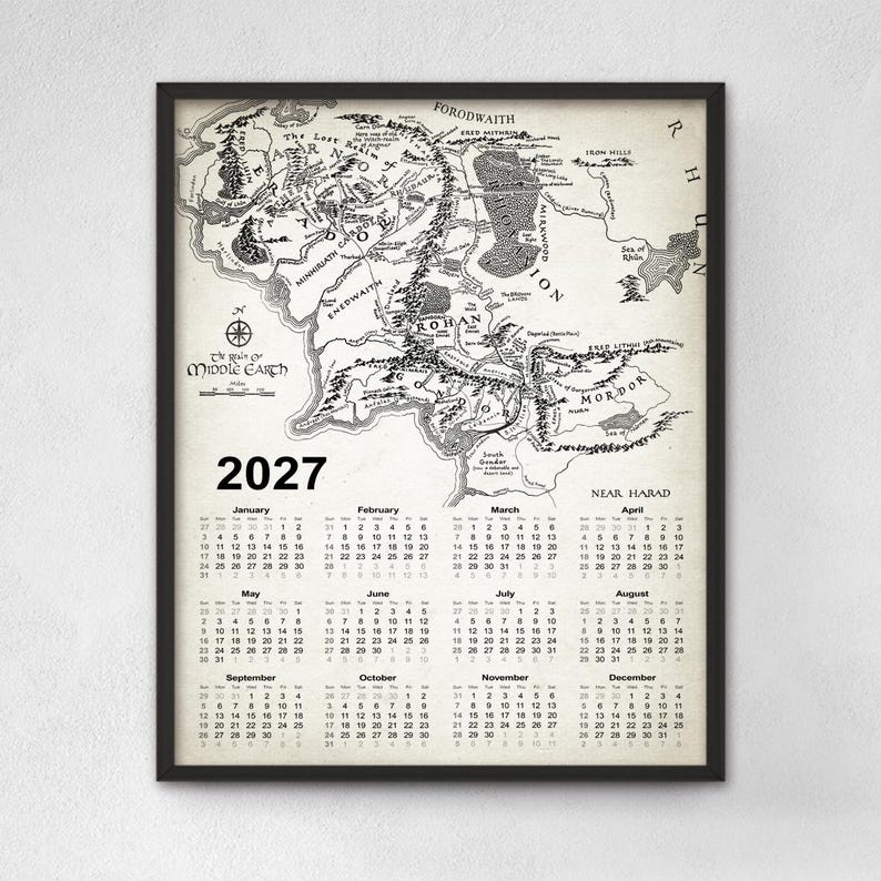 May include: A framed wall calendar for the year 2027 featuring a detailed black and white map of Middle-earth. The top section displays the cartographic illustration with place names, while the bottom section lists the twelve months of the year.