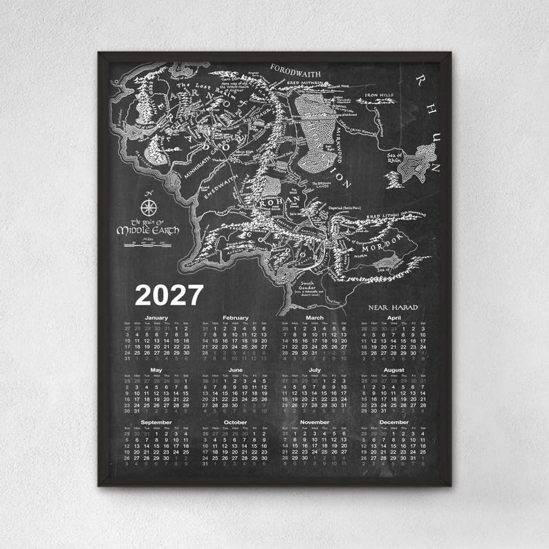 May include: A framed wall calendar for the year 2027 featuring a detailed black and white map of Middle-earth. The top section displays the geographical map with labeled regions, while the bottom section lists the twelve months with dates.