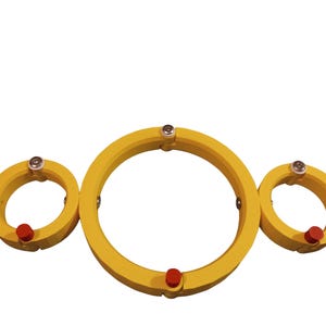 May include: Three yellow circular objects with red and silver accents. The largest ring is in the center, flanked by two smaller rings. The objects appear to be made of a solid material and are set against a white background.