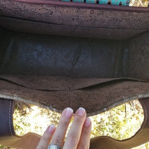 May include: The inside of a brown leather tote bag with a floral pattern. The bag has a brown leather strap and a brown fabric lining.