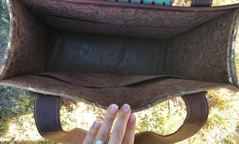 May include: The inside of a brown leather tote bag with a floral pattern. The bag has a brown leather strap and a brown fabric lining.