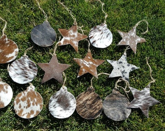 May include: A collection of 15 cowhide ornaments in the shape of stars and ornaments. The ornaments are brown, white, and black with a spotted pattern.