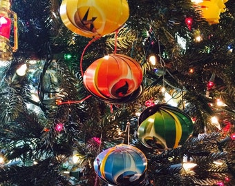 Könnte beinhalten: Ein Weihnachtsbaum, der mit bunten Ornamenten geschmückt ist, darunter eine silberne Kugel, ein gelbes Ornament mit schwarzem Muster, ein rot-oranges Ornament mit schwarzem Muster, ein blau-weißes Ornament mit schwarzem Muster, ein grün-gelbes Ornament mit schwarzem Muster und ein lila-gelbes Ornament mit schwarzem Muster.