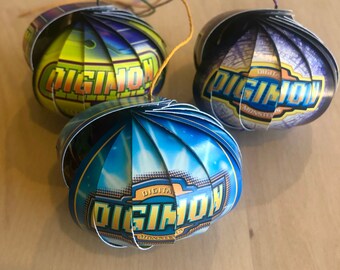 Könnte beinhalten: Drei Digimon-Ornamente, jedes mit einem anderen Farbschema. Die Ornamente bestehen aus gefaltetem Karton und zeigen das Digimon-Logo. Die Ornamente sind blau, grün und lila.