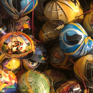 Puede incluir: Primer plano de una colección de adornos hechos a mano y coloridos hechos con cartas de intercambio de Pokémon. Los adornos son esféricos y presentan varios personajes de Pokémon, incluidos Arcanine, Blastoise y Pikachu.