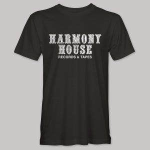 May include: Black t-shirt with the text "HARMONY HOUSE RECORDS & TAPES" in a white, vintage-style font. The shirt has short sleeves and a crew neck. The design is centered on the front of the shirt.