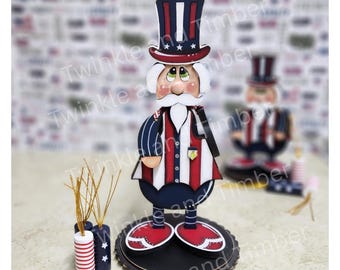 May include: A wooden Uncle Sam figure wearing a top hat, a red and white striped waistcoat, and blue trousers. The figure stands on a black, scalloped base. Small, decorative firecracker ornaments are also visible.
