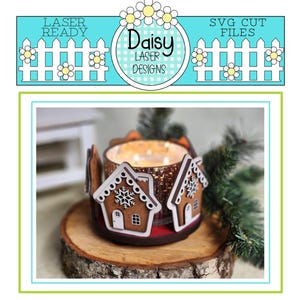 May include: A wooden gingerbread house candle holder with a clear glass candle jar inside. The candle holder is decorated with white icing and a snowflake design. The candle jar is lit and glowing. The candle holder is sitting on a wooden log slice.
