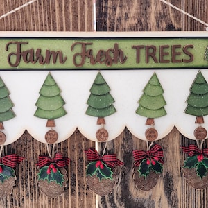 Puede incluir: Cartel de madera con el texto "Farm Fresh TREES" en letras marrones sobre un fondo verde. El cartel presenta cinco árboles de Navidad verdes y adornos decorativos de piñas con lazos rojos y acebo.