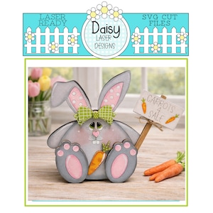May include: A wooden bunny figure with grey and pink accents, holding a sign that reads "Carrots 4 Sale." The bunny has a green bow and is next to a few real carrots. The image also includes the text "Laser Ready" and "SVG Cut Files."