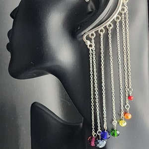 May include: Silver ear cuff with cascading chains and colorful faceted beads. The ear cuff wraps around the ear and features a series of dangling chains, each ending with a different colored bead, creating a rainbow effect.