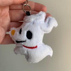 Puede incluir: Llavero de peluche blanco de Zero de The Nightmare Before Christmas. El llavero presenta el dise&ntilde;o del perro fantasma de Zero con ojos negros, un collar rojo y una nariz amarilla. Est&aacute; unido a un anillo de metal plateado.