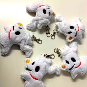 Puede incluir: Cinco llaveros de peluche blanco con forma de perro, con ojos negros, un collar rojo y una oreja amarilla. Cada llavero tiene un cierre plateado. Los llaveros est&aacute;n hechos de material suave y esponjoso.